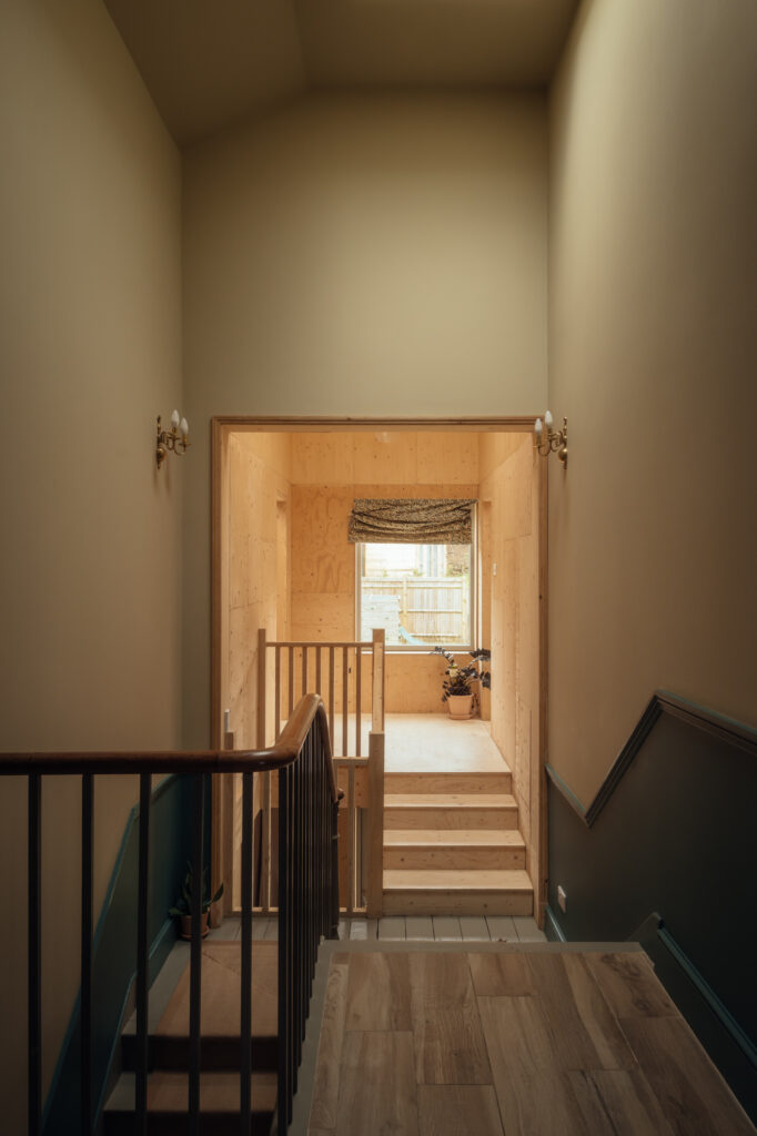 A view from a staircase landing looking into a room with timber cladding and a small set of wooden stairs leading to a window.