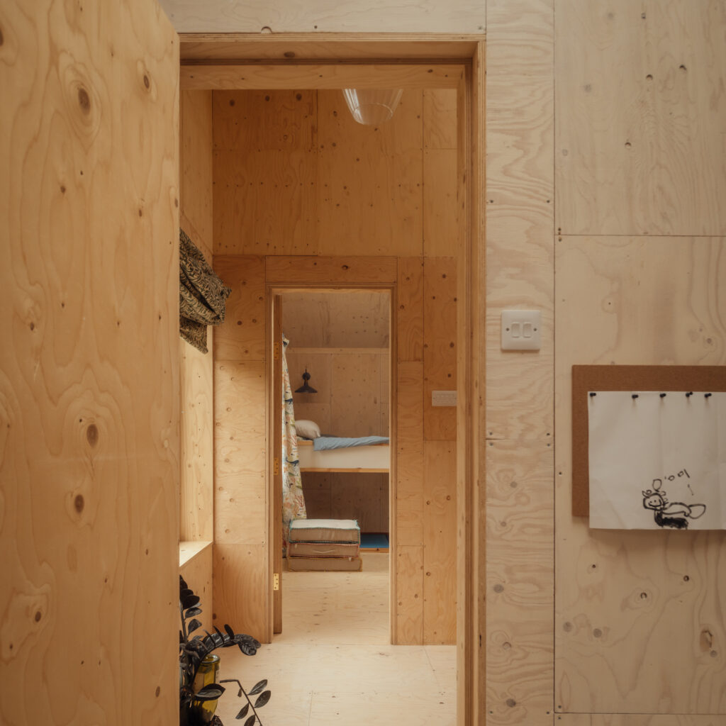 A view through two doorways in a room with light timber cladding, showing a bedroom with a bunk bed in the background.