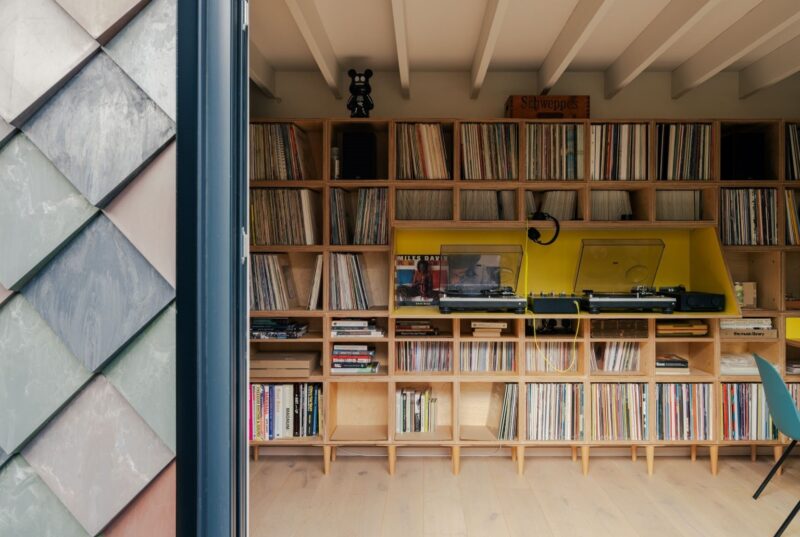 A cosy East London room fitted out with U-Build wooden boxes showcases impressive record storage, featuring a yellow section with two turntables and various audio equipment. Natural light from the left highlights the organised music collection.