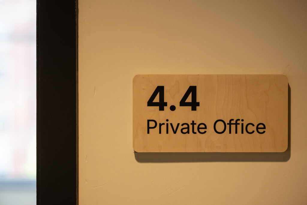 A wooden sign on a beige wall reads 4.4 Private Office, marking the office room number and its designation as a private workspace within Manchester's Sustainable Ventures hub.