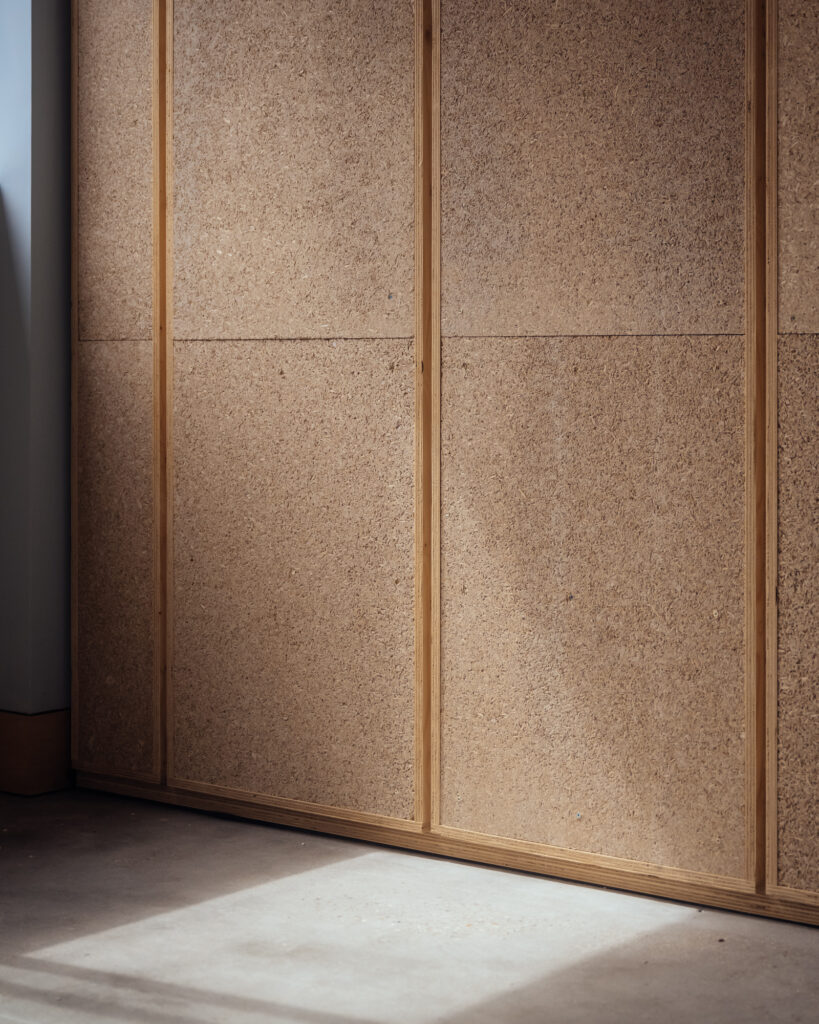 Sunlight streams onto a floor in front of a wall made of light brown cork panels with wooden trim at Vyner Studios. The scene is minimal and softly lit, emphasising the texture of the cork and the simplicity of the space.