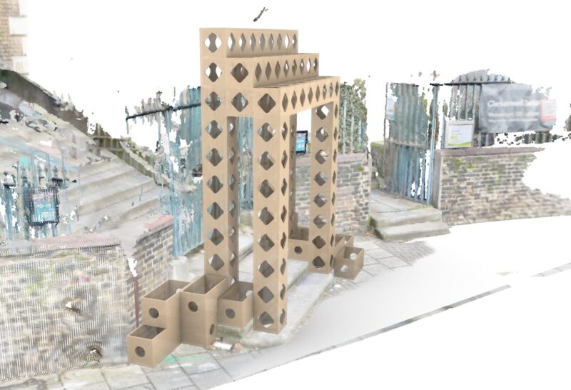 A cardboard archway structure with geometric cut-outs stands on a pavement near brick steps and a metal gate, flanked by cardboard planter boxes—an art installation titled Threshold of Change.